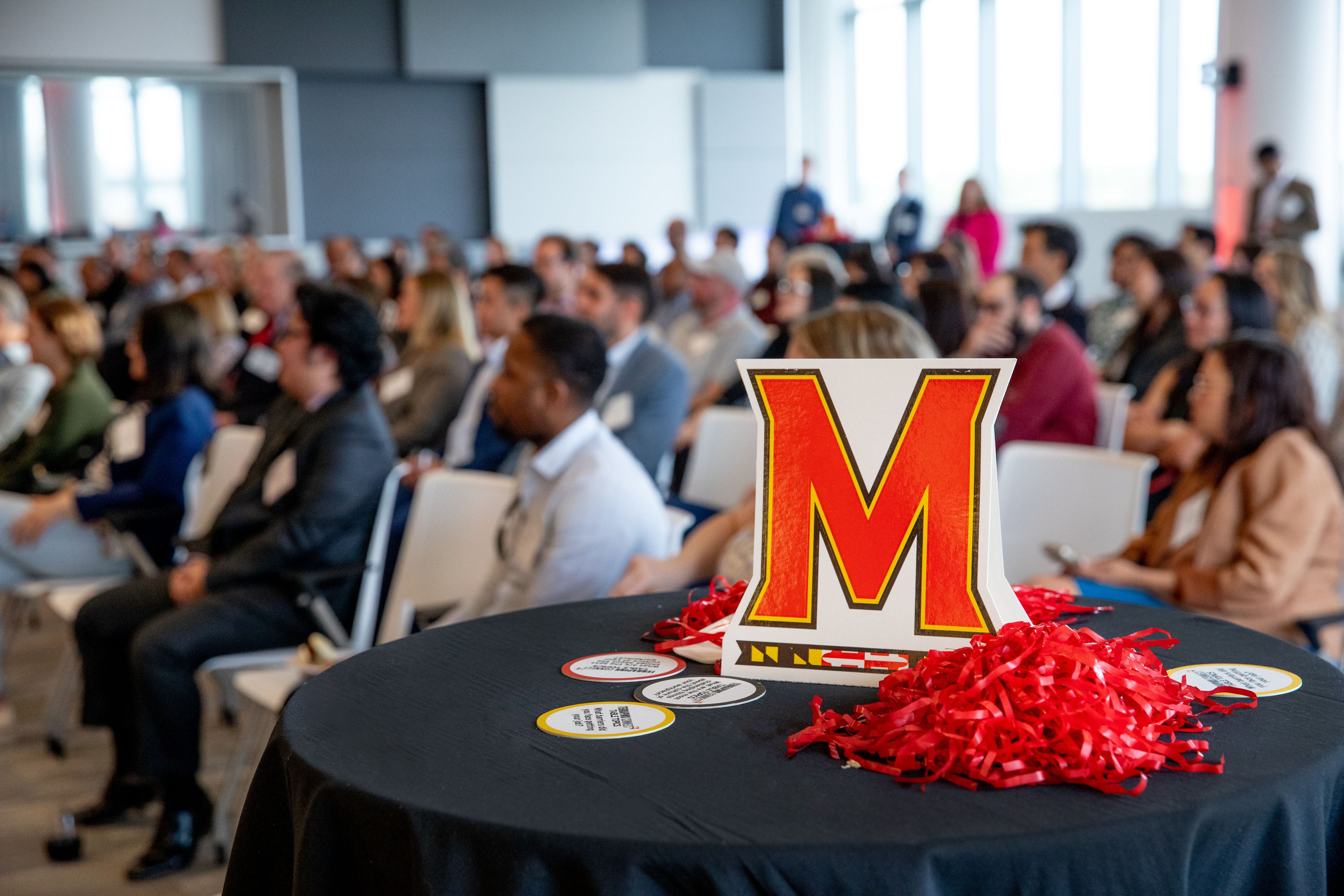 A group of Terp professionals sitting in a meeting room with a Maryland M decoration in the forefront