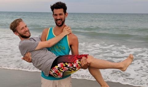 Colin and Michal posing being carried on the beach together.