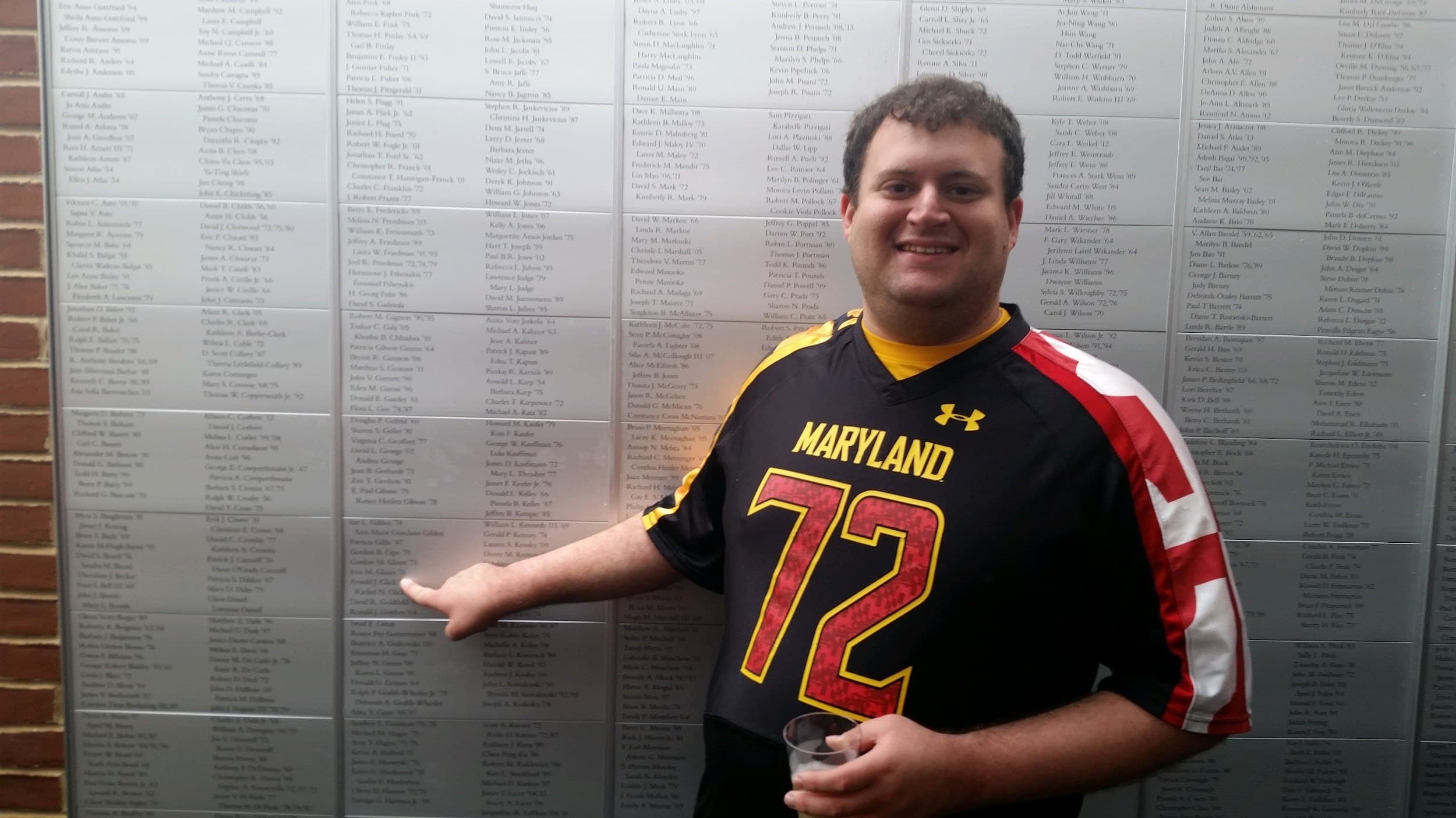 Photo of alum Eric Glazer pointing to his name on the Lifetime Member Wall