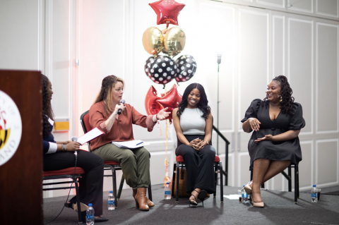 Three women talking on stage at an Alumni Association event.