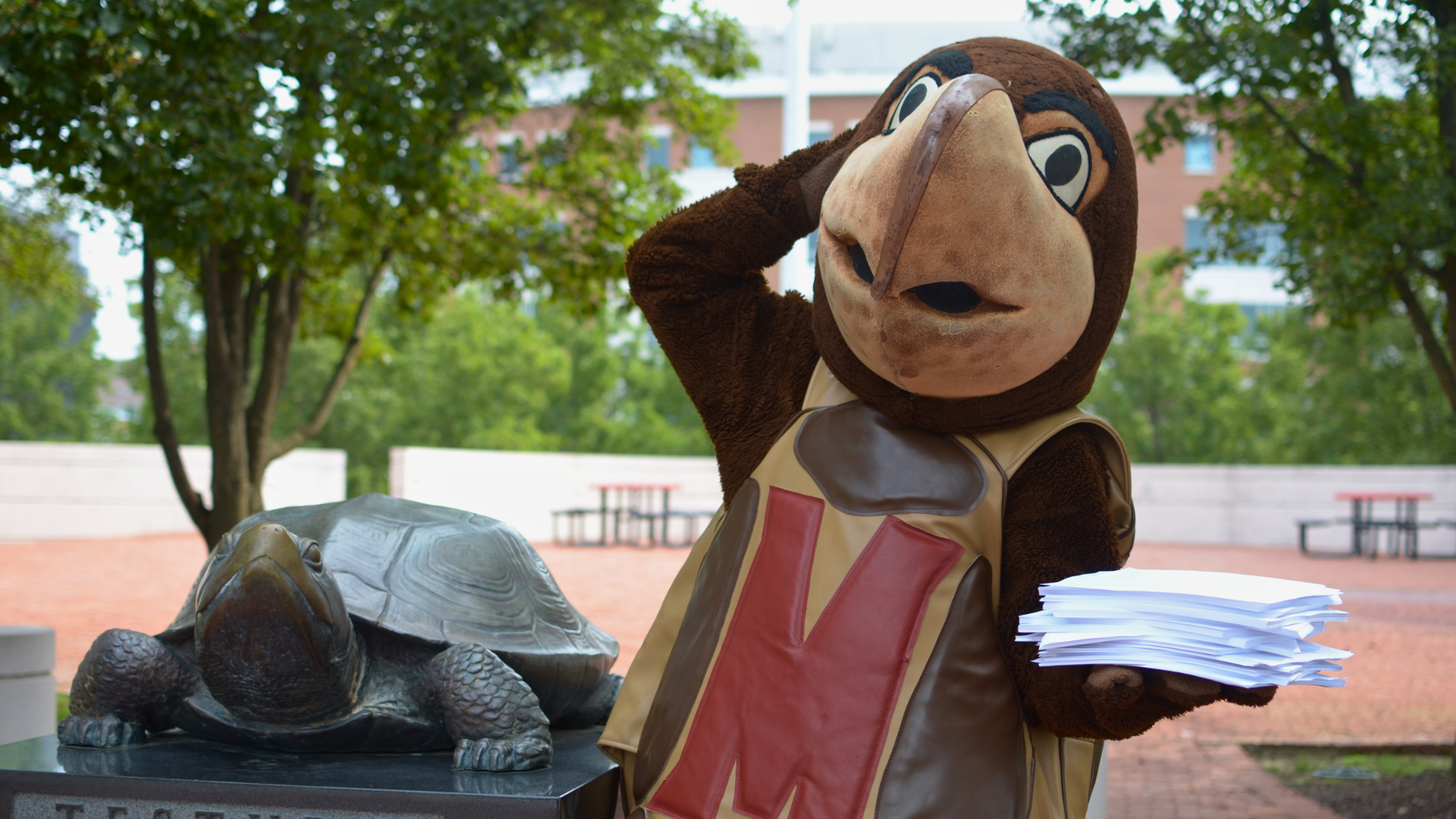 Testudo stands holding a stack of papers toward the viewer