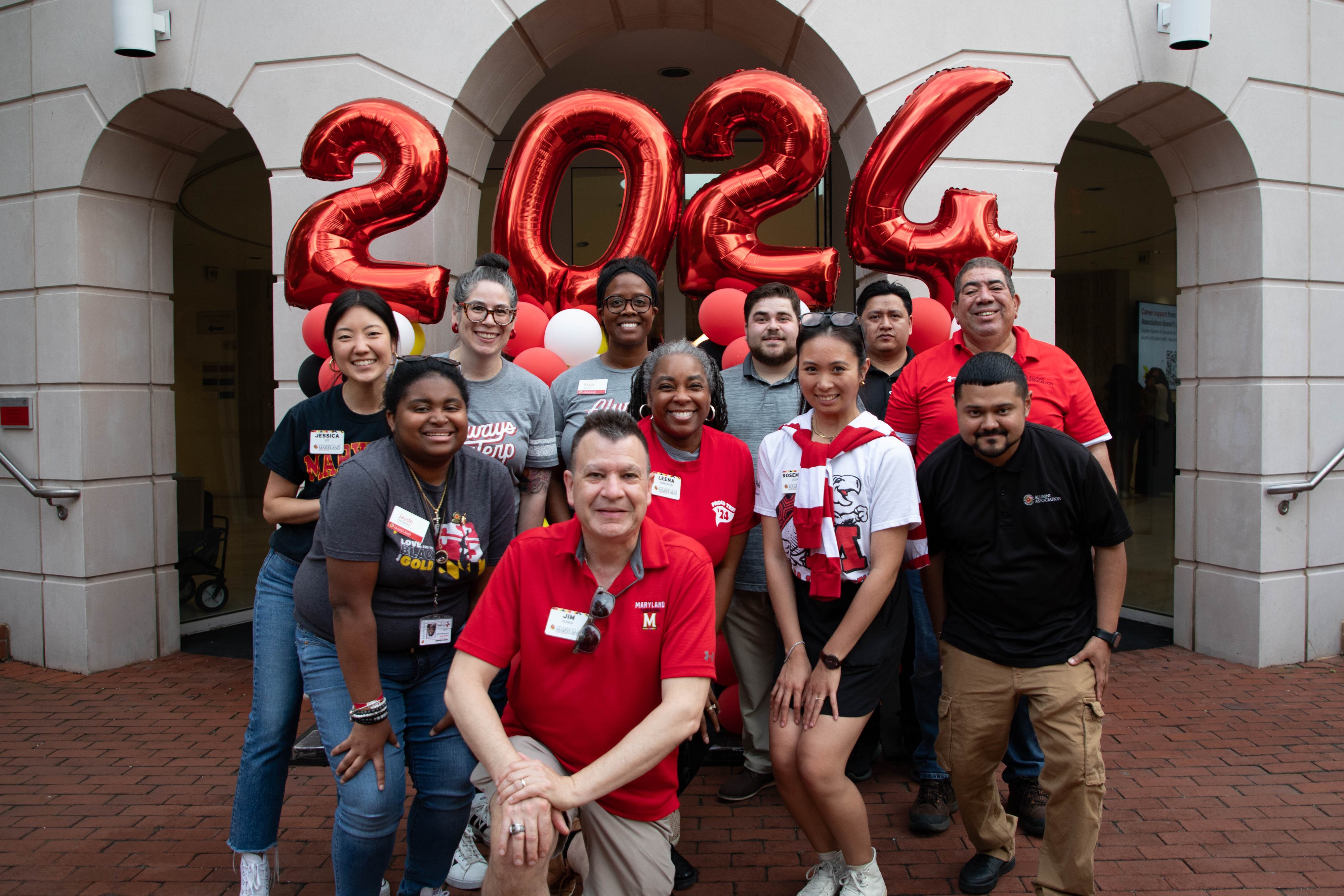 Members of the Alumni Association team pose together with baloons that read 2024