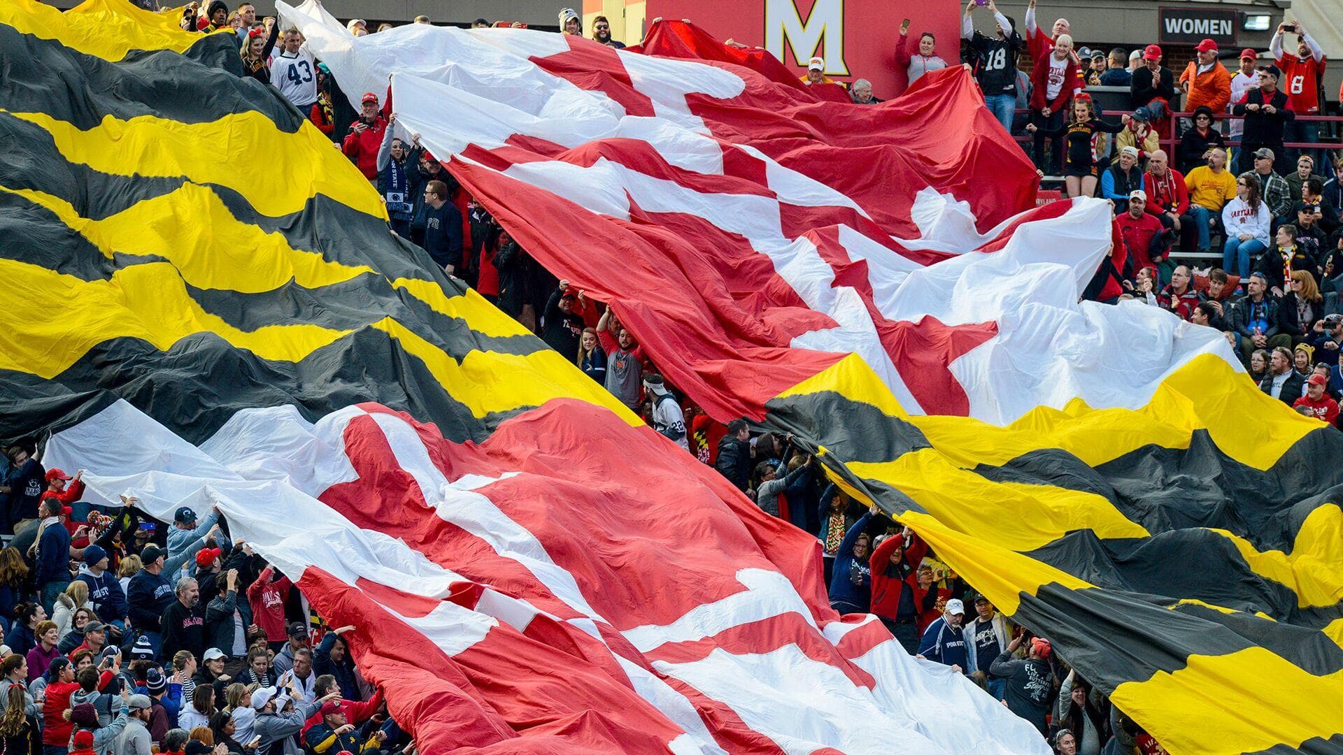 Two huge banners depicting both halfs of the Maryland flag are unfurled over and held up by the crowd of spectators at the University of Maryland home-game at Maryland Stadium