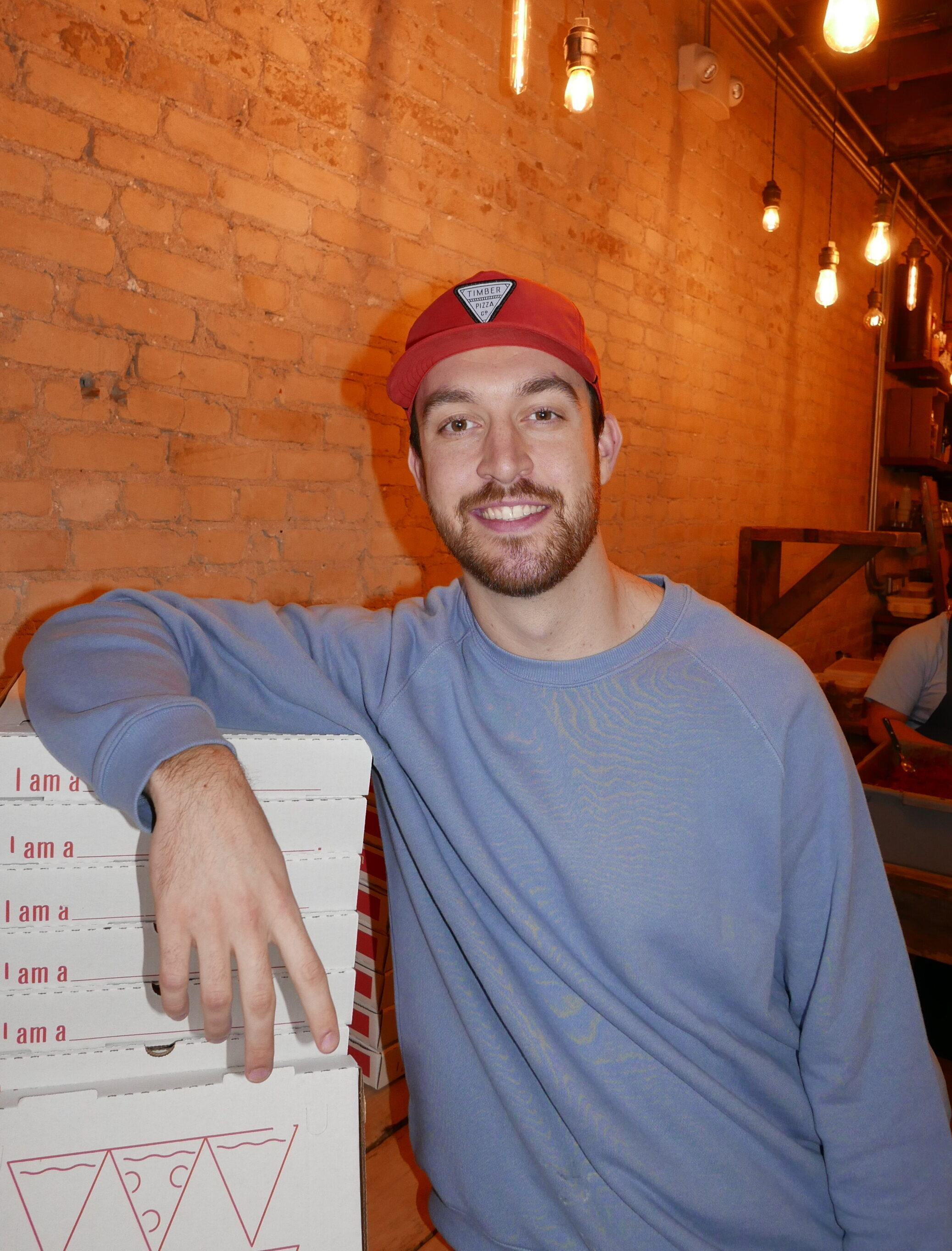 UMD alum Luke Watson '18 poses with a few boxes of Timber's Pizza.