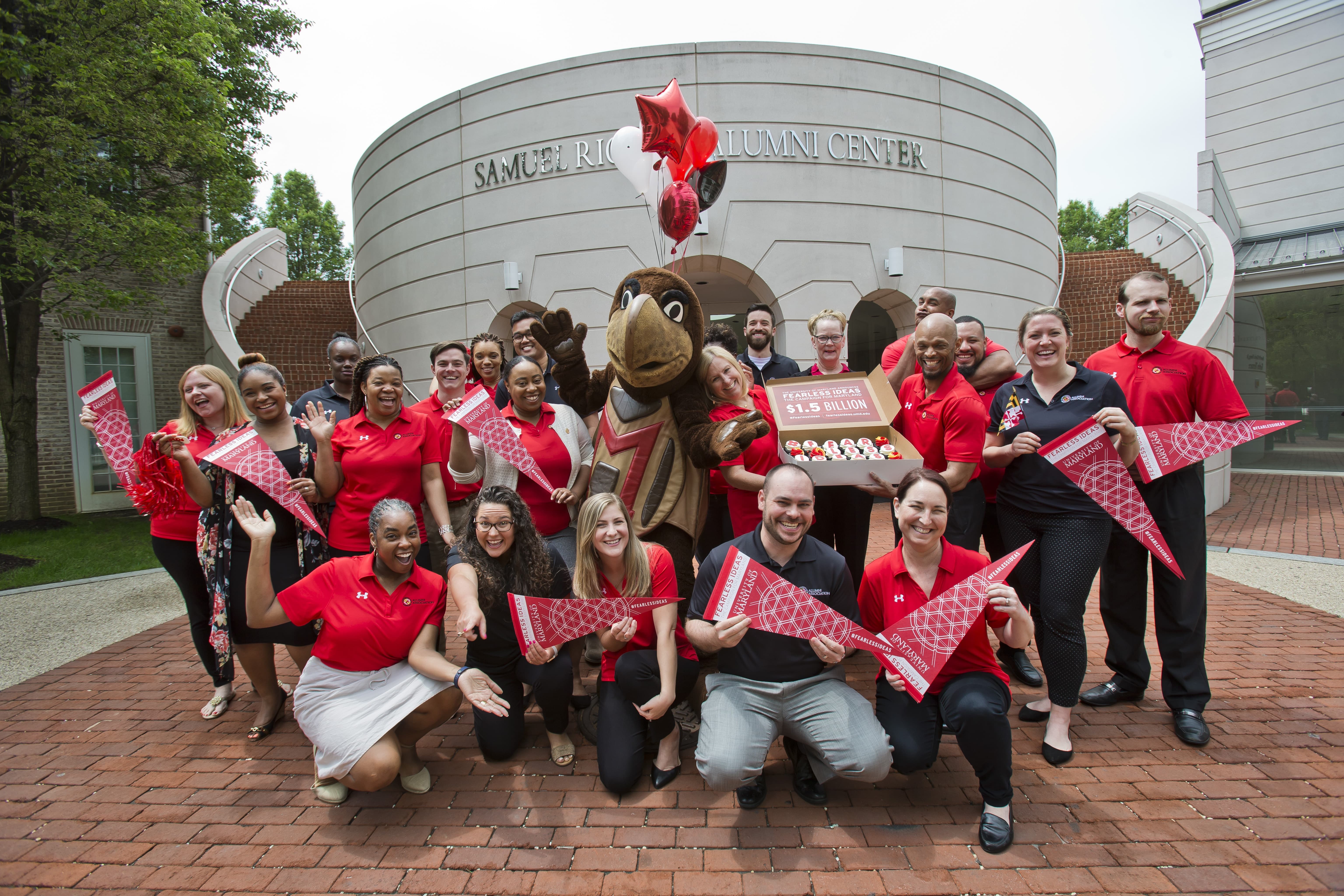 Members of the Alumni Association celebrate reaching the Fearless Ideas Campaign goal with a group photo and cupcakes in front of the Riggs Alumni Center