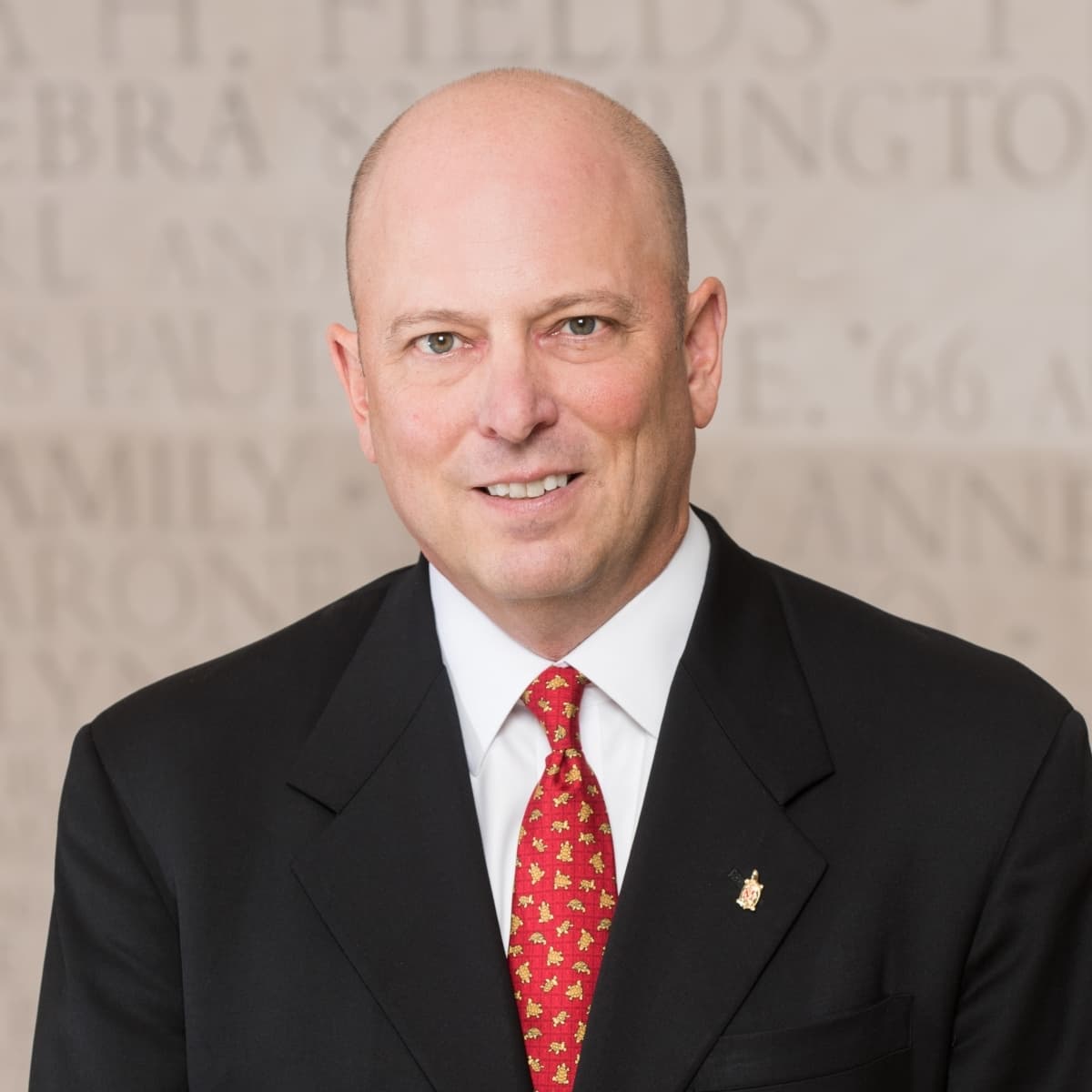 Formal portrait of Jim Spencer in a dark suit, red tie, and testudo turtle lapel pin