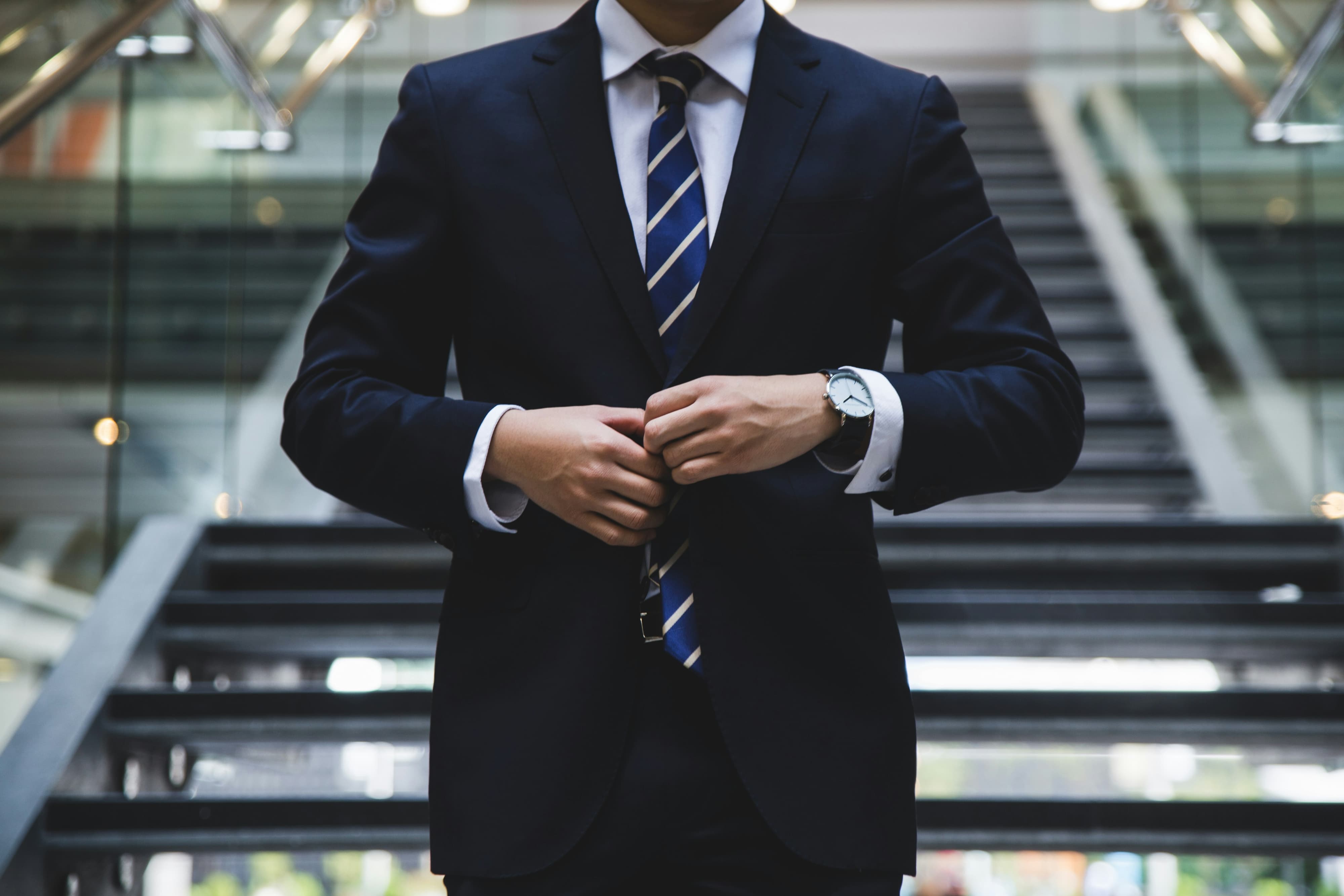 Man dressed in a suit buttoning up his jacket at the bottom of a staircase