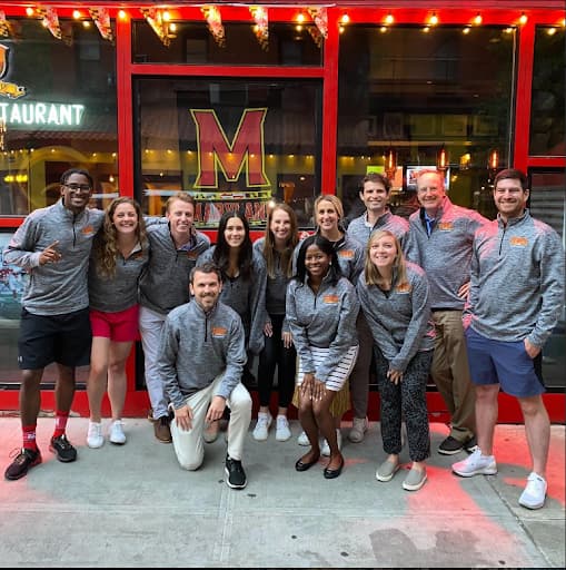 New York Terp Alumni Network members posing outside of a restaurant with a Maryland M behind them