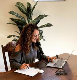 Nassim Ebrahimi '00 taking notes on a notebook while looking at her computer